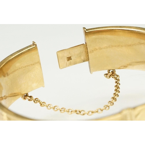 65 - 9ct gold hallmarked bangle bracelet having a hinged mechanism and engraved foliate details to the si... 