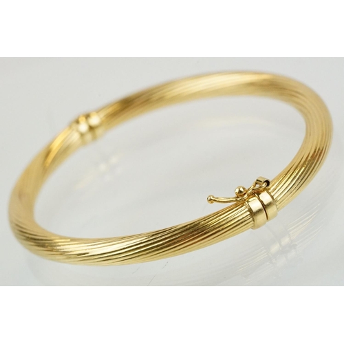 75 - Hallmarked 18ct gold hinged bangle bracelet having a reeded twist design with catch to the clasp. Me... 