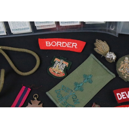 75 - A collection of mixed military collectables to include cloth badges, shoulder titles, lanyards, ciga... 