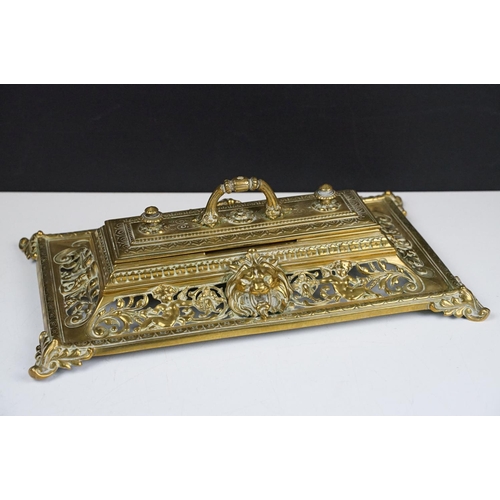 106 - Cast brass inkstand with ornate scrolling and lion mask detail, with hinged cover, approx 35cm wide