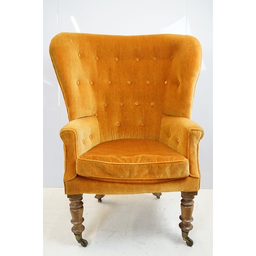 654 - Early 20th century wing back armchair of curved form, with button back, upholstered in orange, on tu... 