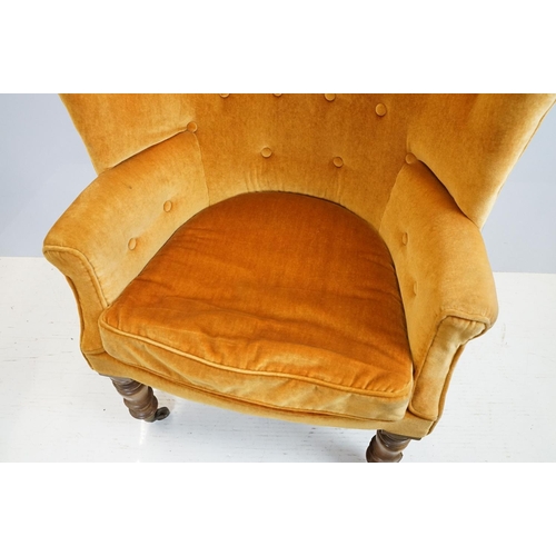 654 - Early 20th century wing back armchair of curved form, with button back, upholstered in orange, on tu... 