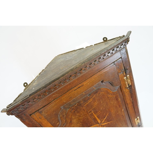 697 - Georgian oak corner cupboard, with dentil cornice above panelled door with parquetry geometric star ... 