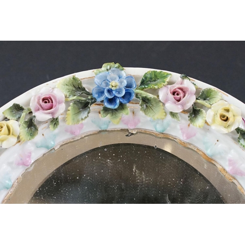 41 - Continental porcelain floral encrusted wall mirror with bevelled glass and two putti to base, hand p... 