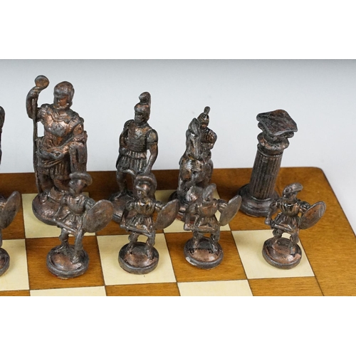 341 - A set of cast metal chessmen in the form of Romans together with a wooden chessboard.