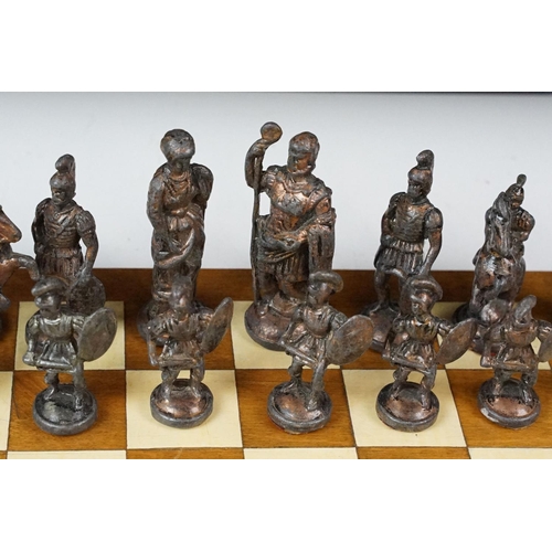 341 - A set of cast metal chessmen in the form of Romans together with a wooden chessboard.