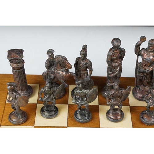 341 - A set of cast metal chessmen in the form of Romans together with a wooden chessboard.