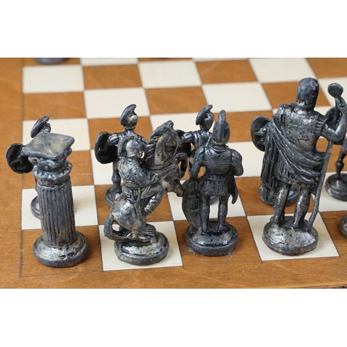 341 - A set of cast metal chessmen in the form of Romans together with a wooden chessboard.