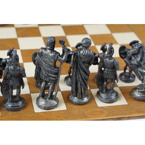 341 - A set of cast metal chessmen in the form of Romans together with a wooden chessboard.