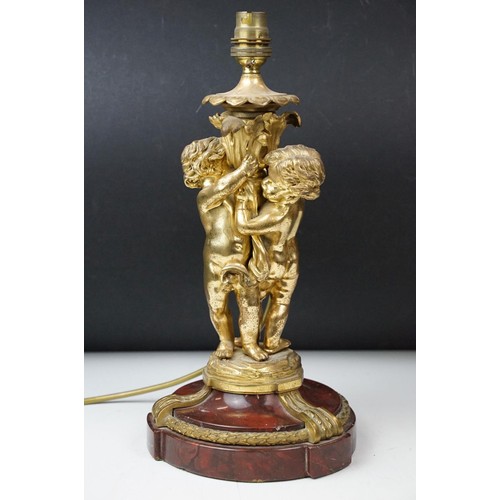 185 - Gilt metal table lamp modelled as two putto, with a red marble base with gilt metal mounts (detached... 