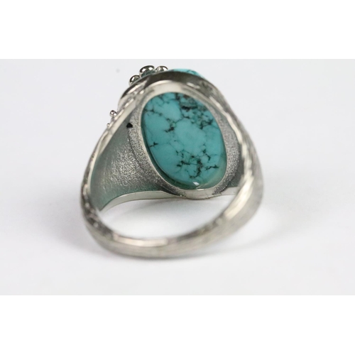 217 - Silver and turquoise ring being set with an oval cabochon to centre with floral detailing and textur... 