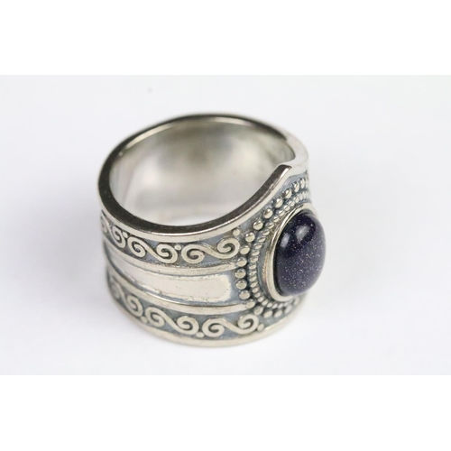 221 - Silver and blue glass ring set with an oval cabochon to the centre with scrolled details to band. Ma... 