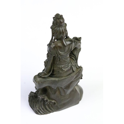 260 - Cast bronze figurine in the form of Guanyin seated on a rock. Measures 11.5cm tall.