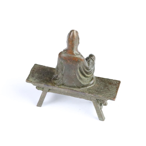 297 - Cast bronze Guanyin Buddha figurine modelled seated on a bench. Measures 8.5cm tall.