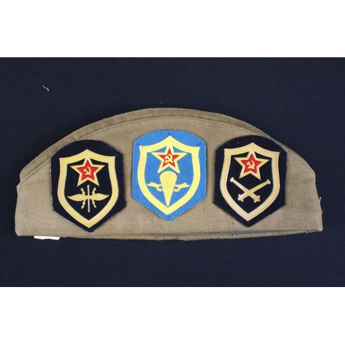 158 - A collection of Russian propaganda badges mounted to military side cap.