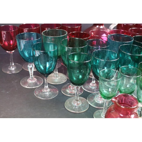 59 - Large selection of green (20) and cranberry (12) clear stemmed glasses with small pouring jugs and c... 