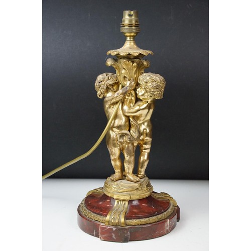 146 - Gilt metal table lamp modelled as two putto, with a red marble base with gilt metal mounts (detached... 