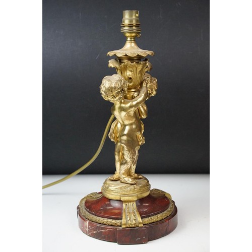 146 - Gilt metal table lamp modelled as two putto, with a red marble base with gilt metal mounts (detached... 