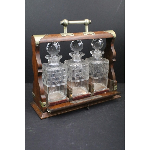 128A - Early 20th century oak tantalus with three glass bottles, with key, 34.5cm high