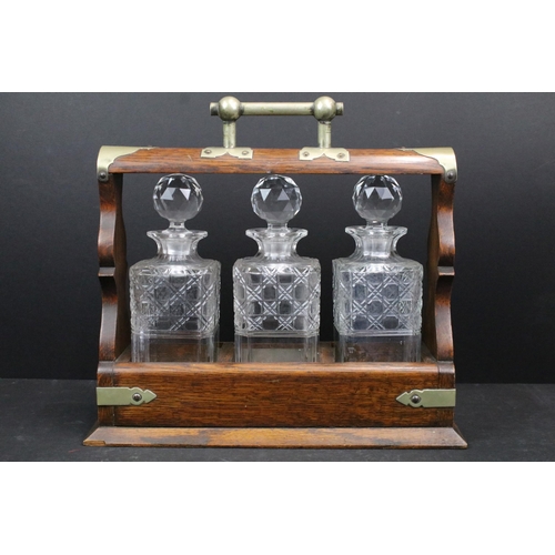 128A - Early 20th century oak tantalus with three glass bottles, with key, 34.5cm high