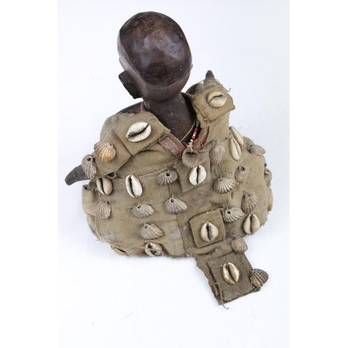 324 - Carved African sculpture of crouching male with hat, adorned with beads, bell, shells and seed pods