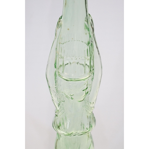 147 - Novelty green glass genie bottle in the form of a woman holding a bottle, 91.5cm high