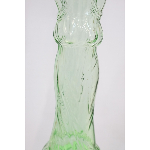 147 - Novelty green glass genie bottle in the form of a woman holding a bottle, 91.5cm high