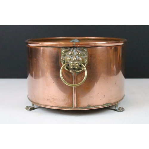 131 - Copper oval planter with rolled rim, brass lion mask drop ring handles and raised on four brass paw ... 