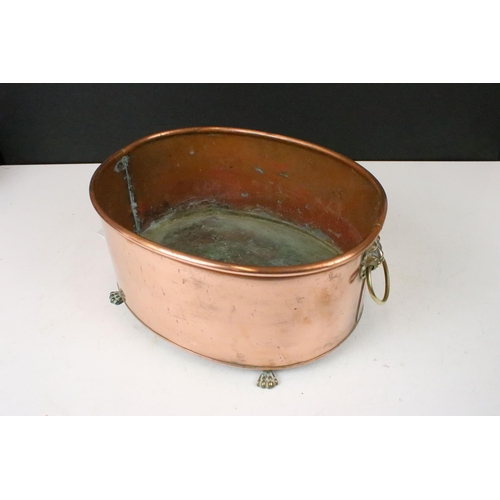 131 - Copper oval planter with rolled rim, brass lion mask drop ring handles and raised on four brass paw ... 