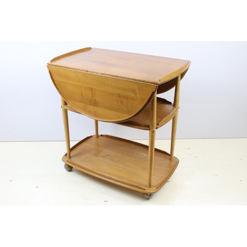 603 - Ercol elm three-tier hostess trolley, the top with two drop leaves, on casters, 76cm high x 95cm wid... 