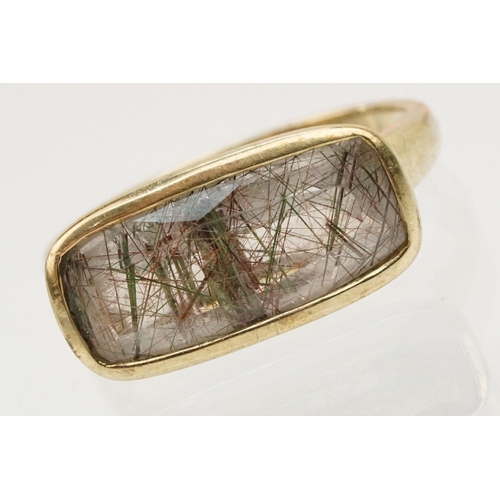 240 - 9ct gold and rutilated quartz ring. The ring being bezel set with a mixed cut rectangular stone on a... 