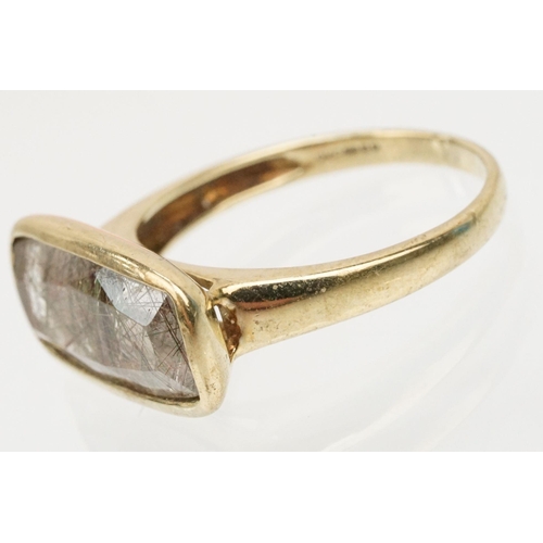 240 - 9ct gold and rutilated quartz ring. The ring being bezel set with a mixed cut rectangular stone on a... 