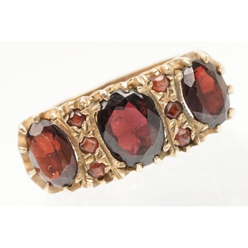 98 - 9ct gold and garnet ring being set with three oval cut garnets with round cut accent stones. Hallmar... 