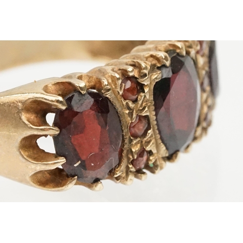 98 - 9ct gold and garnet ring being set with three oval cut garnets with round cut accent stones. Hallmar... 