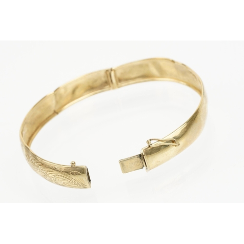 184 - 9ct gold hinged bangle bracelet engraved with foliate scrolls. Marked 375. Measures 5.8cm wide.