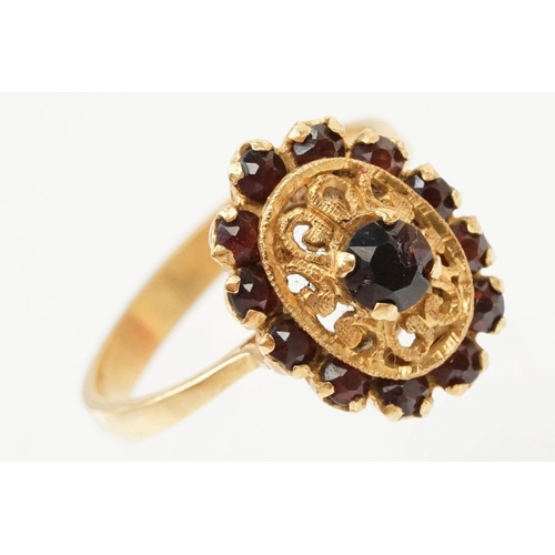 57 - 18ct gold and garnet cluster ring. The ring having a oval head with pierced details, a garnet to cen... 