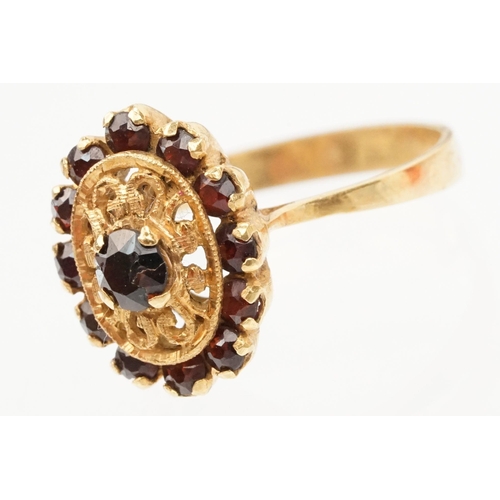 57 - 18ct gold and garnet cluster ring. The ring having a oval head with pierced details, a garnet to cen... 