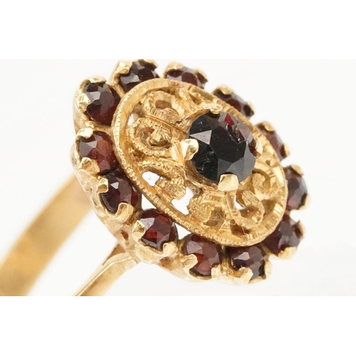 57 - 18ct gold and garnet cluster ring. The ring having a oval head with pierced details, a garnet to cen... 