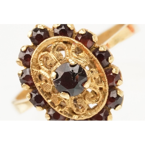 57 - 18ct gold and garnet cluster ring. The ring having a oval head with pierced details, a garnet to cen... 