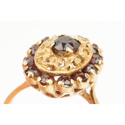 57 - 18ct gold and garnet cluster ring. The ring having a oval head with pierced details, a garnet to cen... 