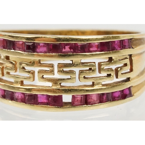 167 - 18ct gold and ruby ring having a pierced Greek key design head with two rows on channel set step cut... 