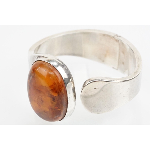 175 - Silver and amber bangle bracelet having a large amber cabochon to the head and hinged opening to the... 