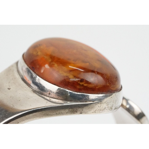 175 - Silver and amber bangle bracelet having a large amber cabochon to the head and hinged opening to the... 