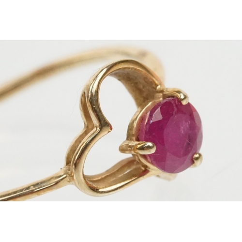 252 - 9ct gold and ruby ring. The ring being set with a round cut ruby within a pierced heart head on a pl... 