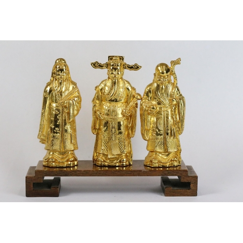 266 - Three gilt metal Chinese figures with wooden stand together with two gilt eggs.