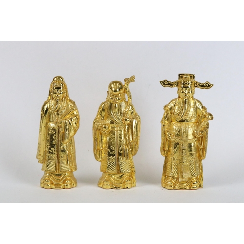 266 - Three gilt metal Chinese figures with wooden stand together with two gilt eggs.