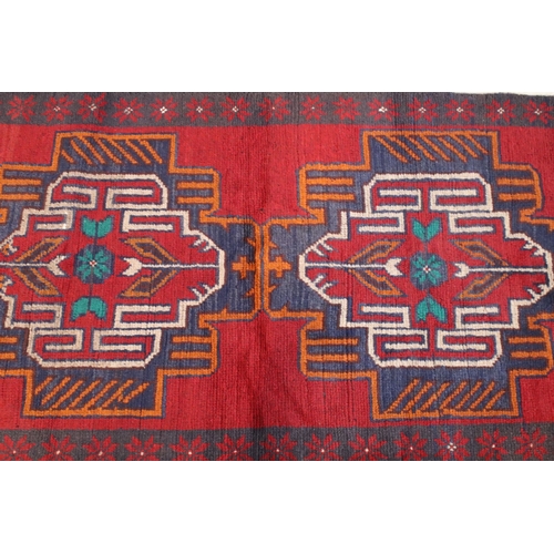 634 - Baluchi rug having a red ground with two geometric medallions to the central panel, 152cm x 88cm