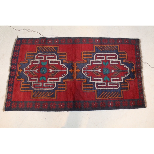 634 - Baluchi rug having a red ground with two geometric medallions to the central panel, 152cm x 88cm