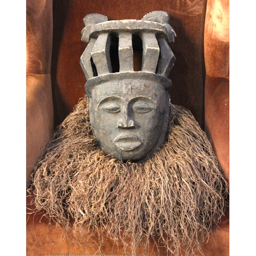 172 - An African tribal mask, the carved wood face wearing a crown, and with raffia fringe, 20th century, ... 