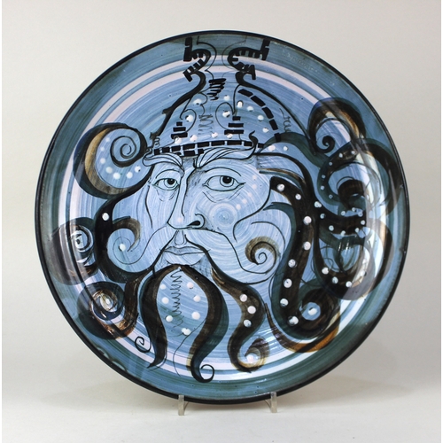 93 - A Robert Melville studio pottery charger decorated with the head of a bearded warrior in blue glazes... 